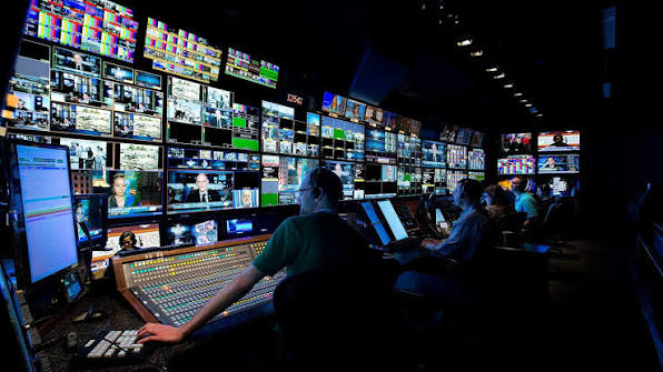 Television producers working at a broadcast control room console